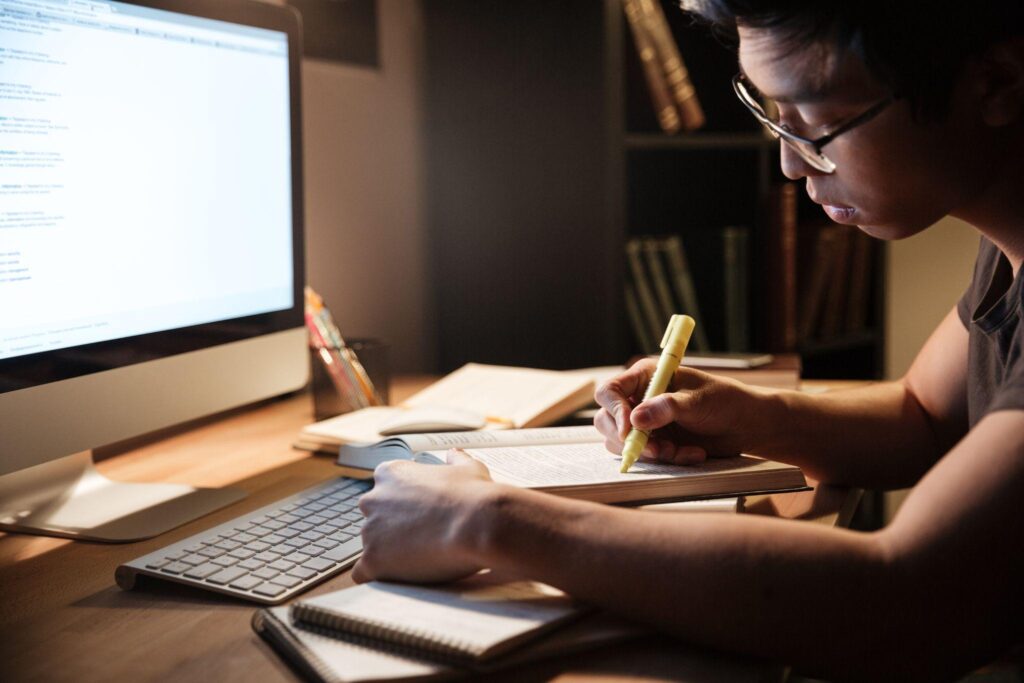 asian young man studying with books and computer in dark room at home