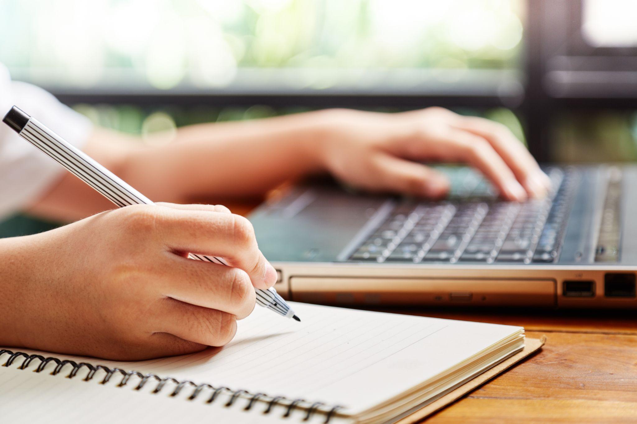hand of girl writing some data in notebook while studying online course on computer laptop