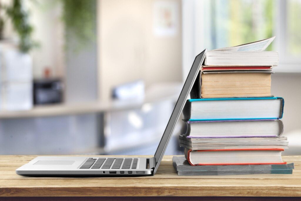 stack of books with laptop on wooden table