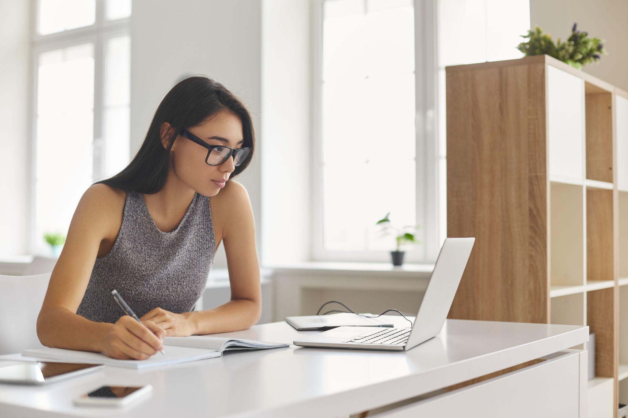 student writing in notebook and using laptop computer for e-learning