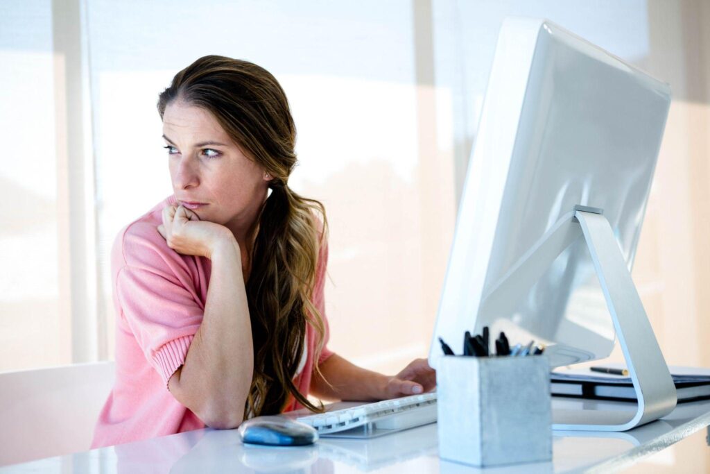 distracted business woman sitting at her desk, looking away from her computer