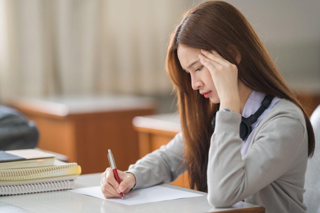Young desperate Asian student in student uniform doing examination assignment
